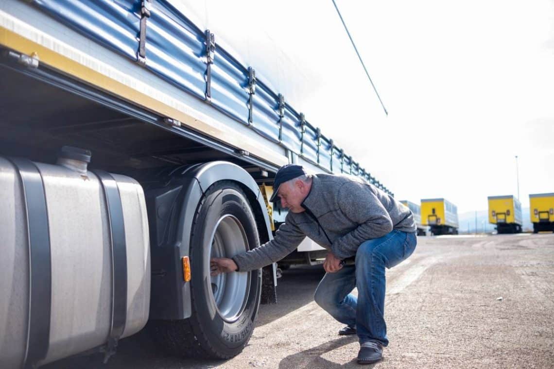Un chauffeur poids lourd en train d'inspecter les pneus de son camion